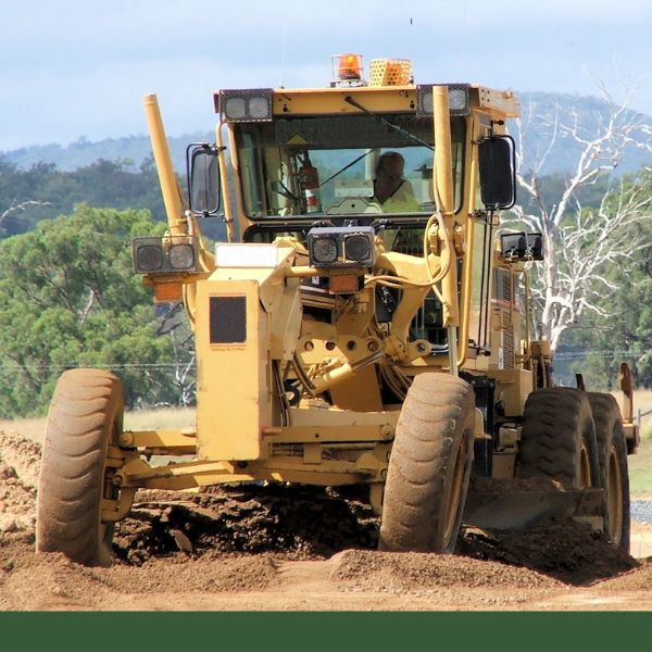 Yellow construction grader moving dirt on a rural road