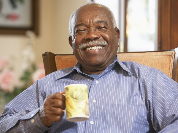 Very happy older Black man holding a mug of coffee and smiling at the camera. 