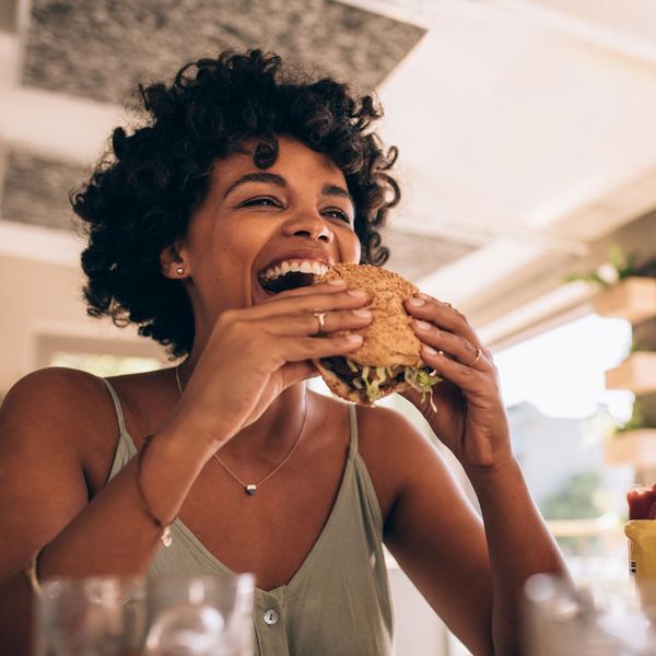 A woman smiling while raising a sandwich to her mouth