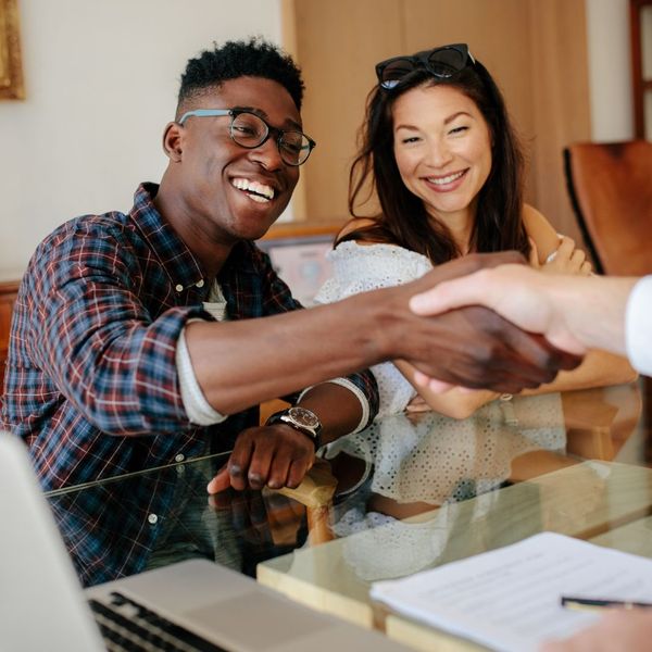 A young man and woman smiling while shaking hands with their realtor