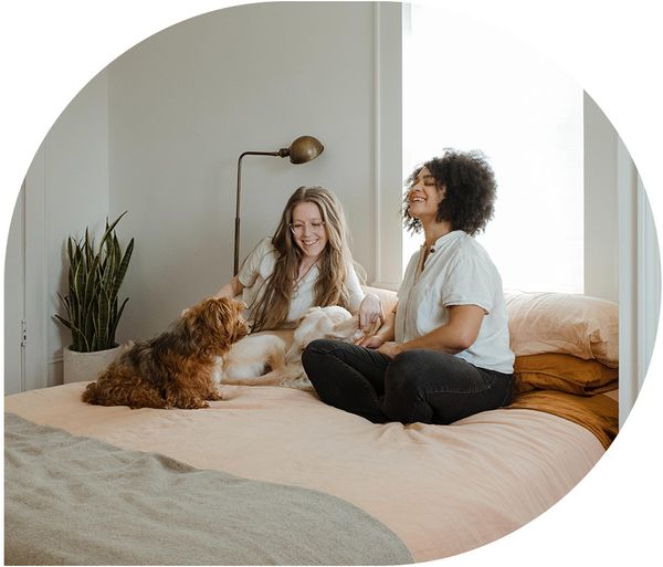 Two women and their dog sitting on a bed laughing