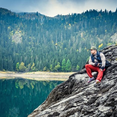 Man sitting on a rock looking over a lake in the mountains.