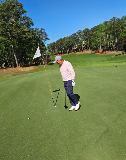 David Sapp, Warrior Golf Academy Board Member, stands near the flagstick on a sunny green, eyeing a putt during a WGA event held at a scenic course lined with tall pine trees. His presence reflects a commitment to supporting veterans through the game of golf. David Sapp Observes Putt on Green During Warrior Golf Academy Event