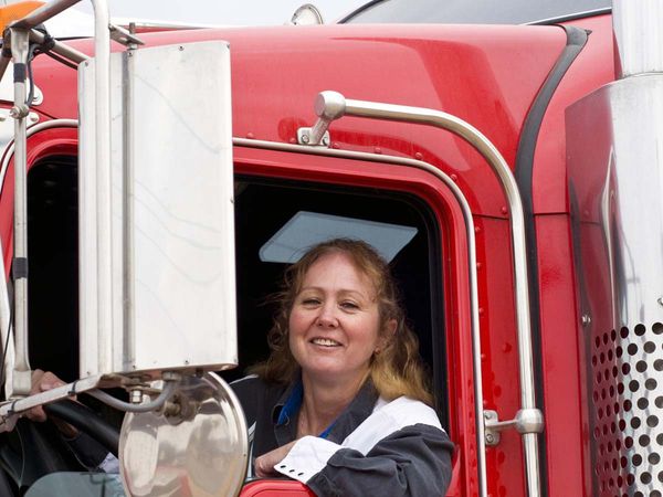 Truck driver leaning out the window of a semi and smiling to the camera. 