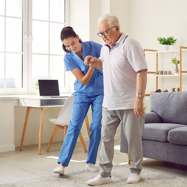 A nurse patiently helping a senior man walk across the room