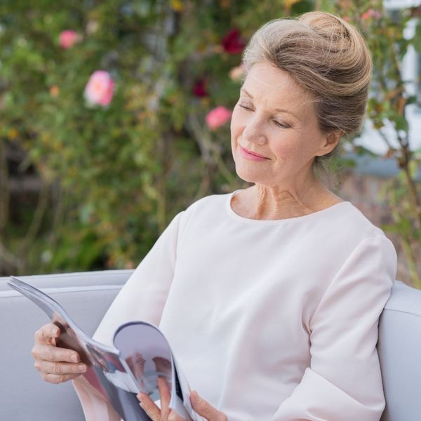 A senior woman sitting while reading a magazine