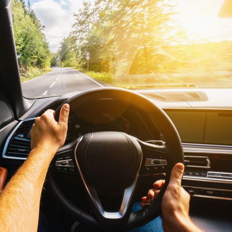 person driving in car with sun shining through windshield