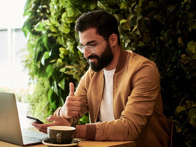 a man giving a thumbs up to his laptop while on his phone