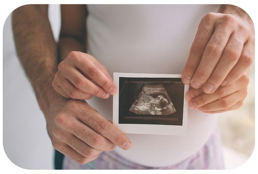 couple holding ultrasound in front of woman's pregnant belly