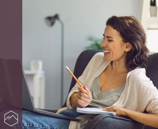 A smiling woman holding a notebook and pencil, looking at her laptop. A smiling woman holding a notebook and pencil, looking at her laptop.