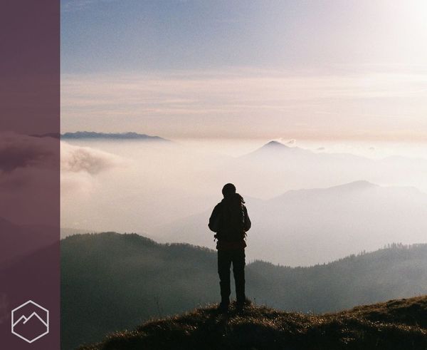 The silhouette of a person standing on a mountain peak, looking at a view of cloudy mountains. The silhouette of a person standing on a mountain peak, looking at a view of cloudy mountains.