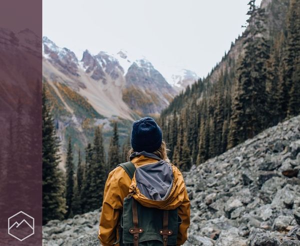 The back of a person with a backpack standing in a rocky valley, looking at snow-covered mountains. The back of a person with a backpack standing in a rocky valley, looking at snow-covered mountains.