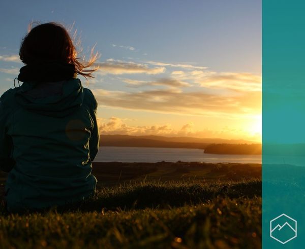 A person sitting on a grassy hill, looking out at a lake during a sunset. A person sitting on a grassy hill, looking out at a lake during a sunset.