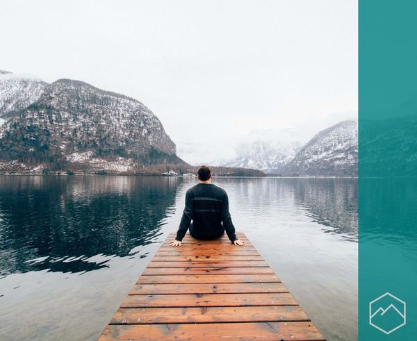 A person sitting on a dock, looking out at a calm lake surrounded by snow-covered mountains. A person sitting on a dock, looking out at a calm lake surrounded by snow-covered mountains.
