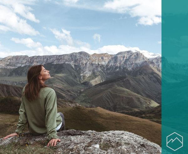 A person sitting on a rock on a mountain overlooking a vast valley. A person sitting on a rock on a mountain overlooking a vast valley.