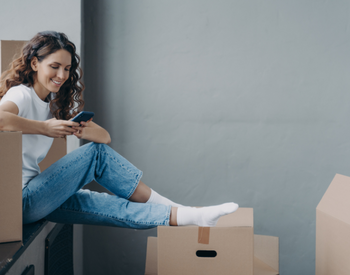 woman smiling while on her phone surrounded by moving boxes