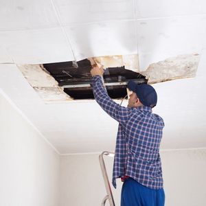 tech fixing a ceiling with water damage