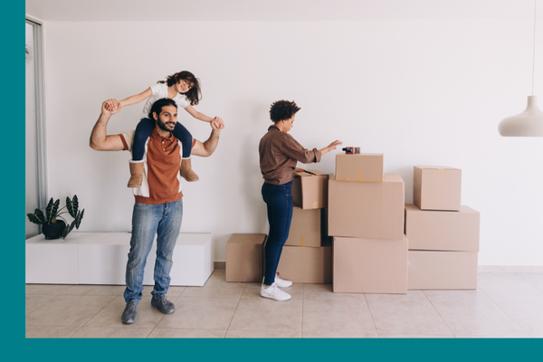 A family standing next to their stack of moving boxes with the daughter on the dad's shoulders