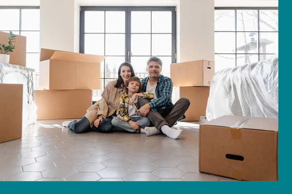 A family sitting on the floor of their new home amidst moving boxes
