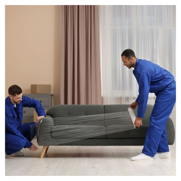 movers in blue jumpsuits wrapping couch in plastic