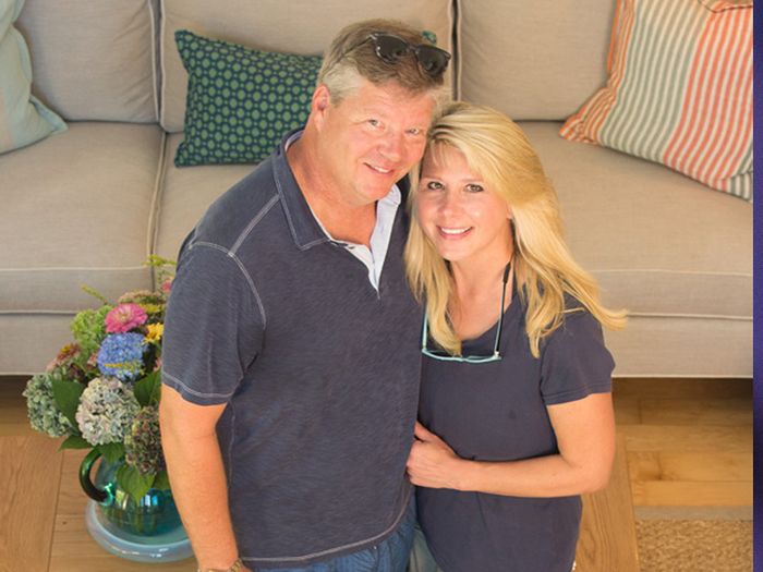 Liisa Holm and her husband standing in their living room with their dog below them