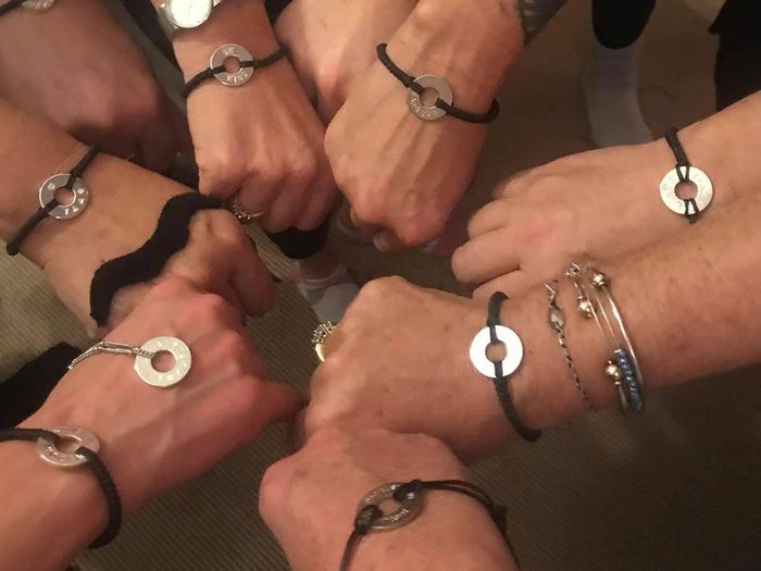 A group of fists “all in” a middle huddle with matching bracelets.