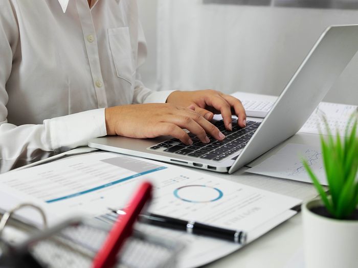 Person typing on laptop with paperwork on the table.