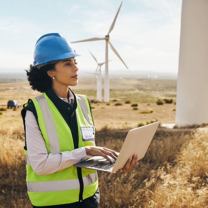 An engineer with her laptop by wind turbines in an open field