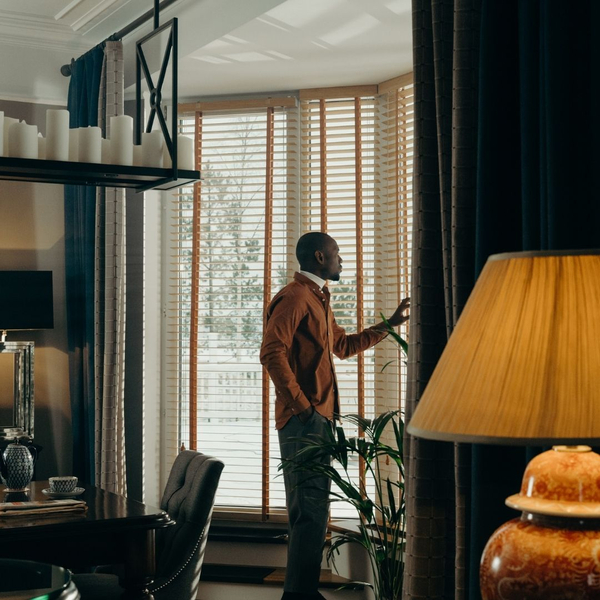 man stands at full height weindows with blinds Why Interior Shutters Are Worth the Investment 2.jpg