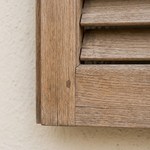 weathered exterior wood shutter joinery, showing hairline cracks in the dry grain that require maintenance