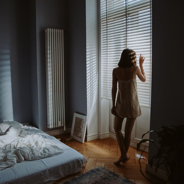woman standing at window in bedroom Why Interior Shutters Are Worth the Investment 3.jpg