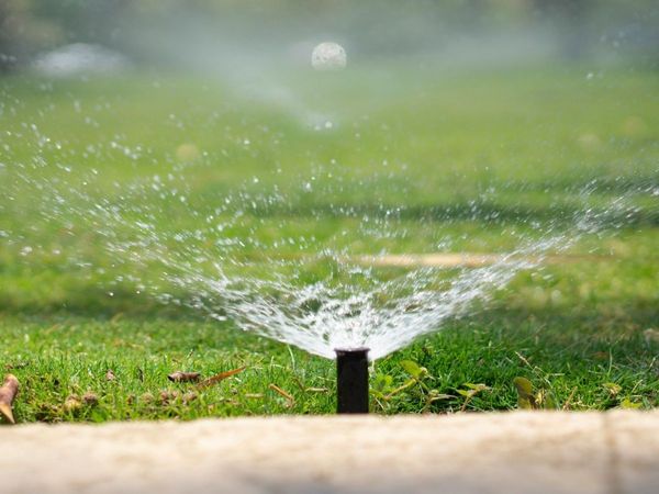 A close-up, ground-level view of a high-performance sprinkler head dispersing a consistent water spray across a healthy, sunlit residential lawn.