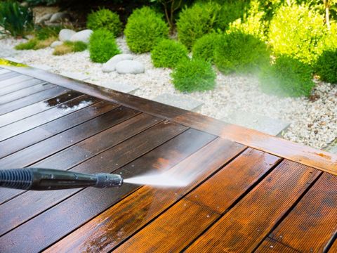 A high-pressure power washing wand cleaning a wooden deck, showing the clear contrast between the dirty surface and the restored wood.