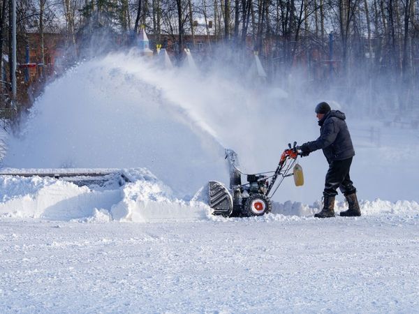 A professional snow removal specialist using a heavy-duty snow blower to clear a large paved area during a heavy Long Island winter.