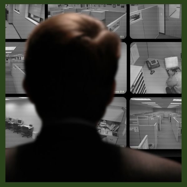 A security operator monitors multiple surveillance camera feeds displaying various office locations.