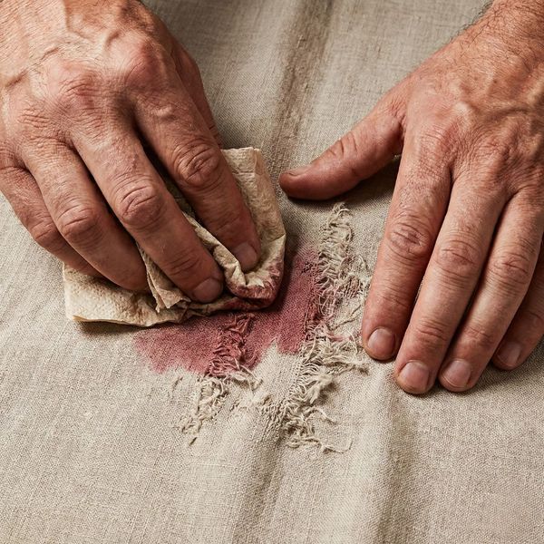 Hands aggressively scrubbing a stain on fabric, causing visible damage to the material.