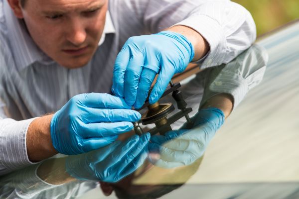 Man leaning in while using a tool to replace a car windshield. 