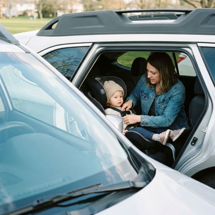 A parent buckling a child into a car seat behind a newly replaced, perfectly clear windshield.