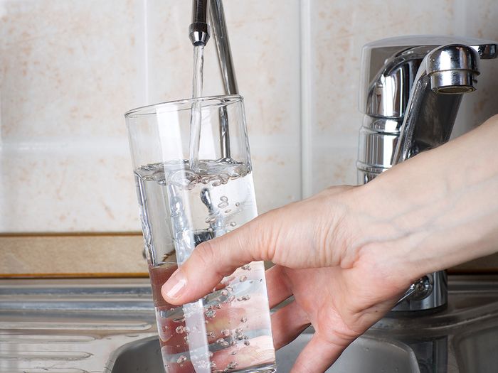 person filling up glass of water at the sink