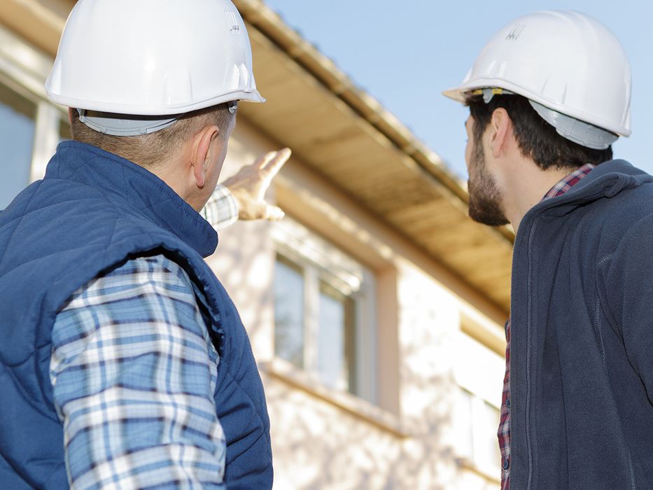 Two men in hard hats pointing to a home. 