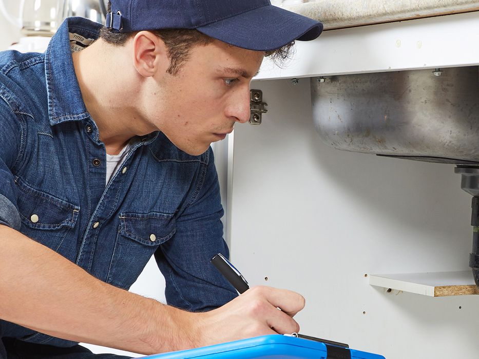 Inspector taking a look at the pipes underneath a sink.