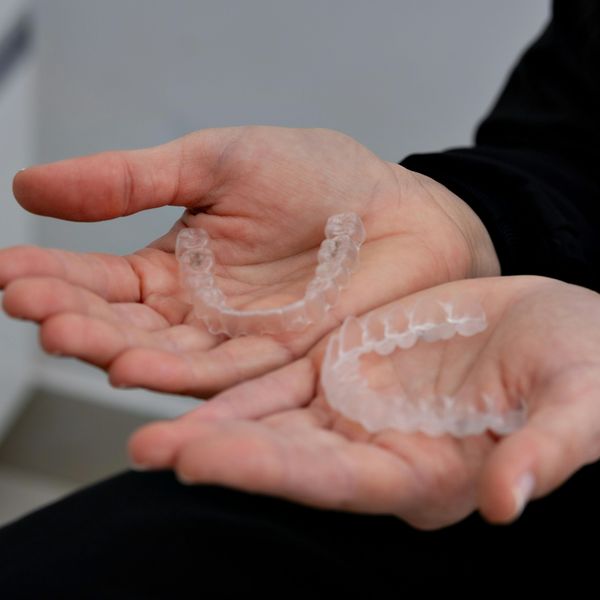 Two clear Invisalign aligners are held in a person's open palms, ready for use.