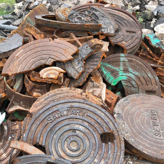 A large pile of broken and rusted old iron manhole covers at a scrap or disposal site. A large pile of broken and rusted old iron manhole covers at a scrap or disposal site.