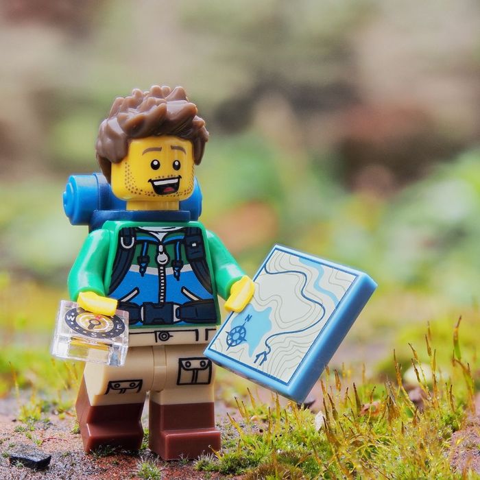 A camping minifig holding a map in the forest