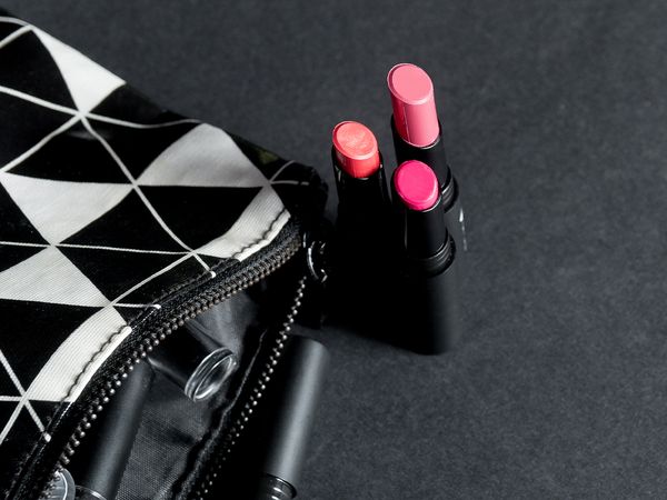 Three different shades of pink lipstick sitting beside a black and white makeup bag. 