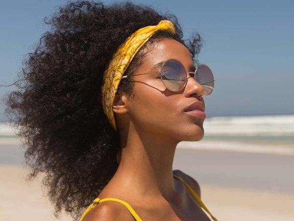 African American woman with beautiful, curly hair wearing sunglasses and a yellow headband. 