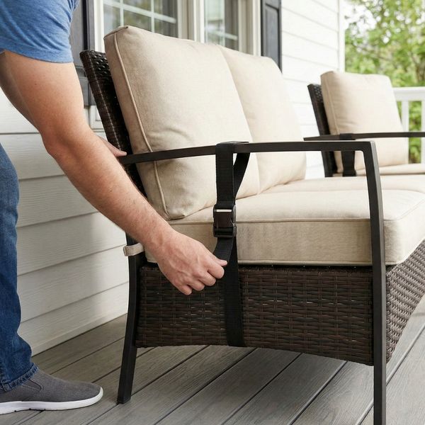 hands tightening a black strap to secure wicker patio furniture on a porch hands tightening a black strap to secure wicker patio furniture on a porch
