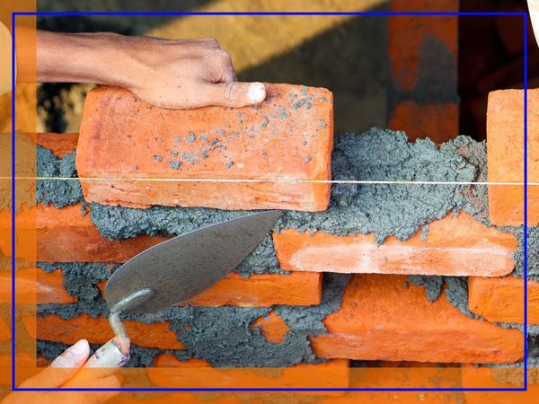 A close-up of hands laying bricks with mortar on a construction site, showing bricklaying in progress. A close-up of hands laying bricks with mortar on a construction site, showing bricklaying in progress.