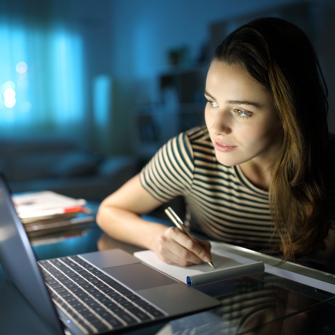 a woman taking notes in front of a laptop at night