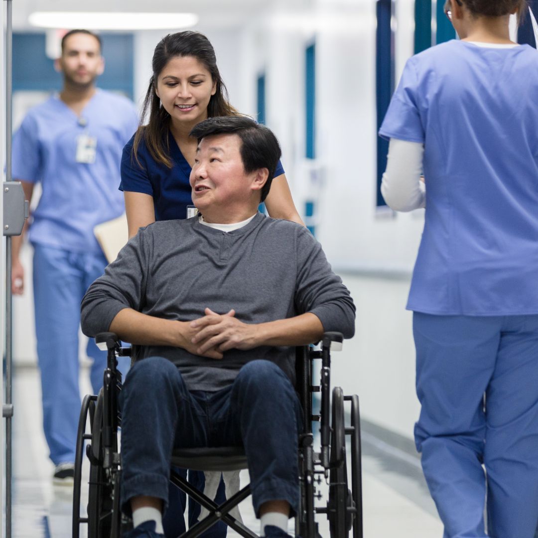 a nurses aid pushing a patient in a wheelchair down a hallway